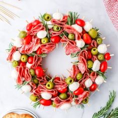 a wreath made out of meat, cheese and olives on a white table with crackers