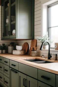 a kitchen with green cabinets and wooden counter tops in front of a window that has potted plants on it