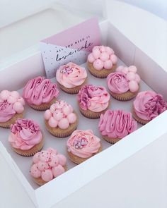 a box filled with pink frosted cupcakes on top of a white table