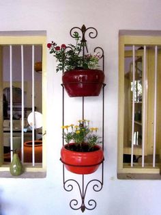 two hanging planters with flowers in them on a wall next to windows and a potted plant