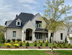 a large white house with lots of trees and bushes around it's front yard