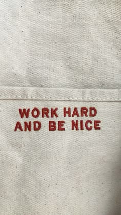 an embroidered work hard and be nice sign on the back of a white jacket with red lettering