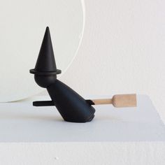 a black object with a wooden stick sticking out of it's side on a white surface