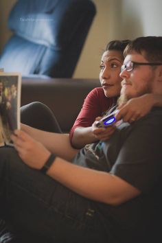 a man and woman sitting on a couch looking at a book with their arms around each other