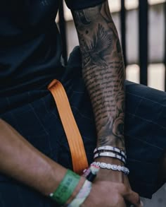 a tattooed man sitting on the ground with his arm wrapped around an orange belt and bracelet