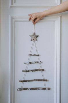 a christmas tree made out of branches hanging on the front door with someone's hand