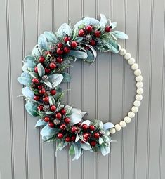 a wreath with red berries and greenery hanging on the wall next to a door