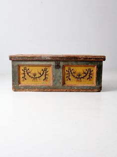 an old wooden box with two yellow painted designs on it's sides, sitting on a white surface