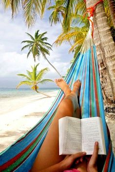 a woman reading a book in a hammock on the beach with palm trees