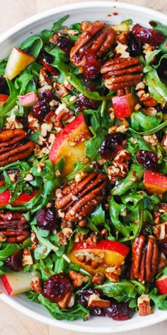 a salad with apples, cranberries, pecans and nuts in a white bowl