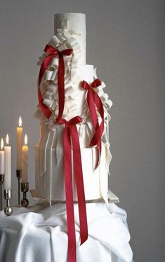 a white wedding cake with red ribbon and candles