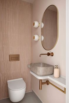 a white toilet sitting next to a bathroom sink under a round mirror on a wall