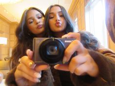 two women taking a selfie in front of a mirror with one holding a camera