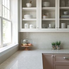 a kitchen with white cabinets and marble counter tops, pots and pans on the shelves