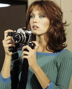 a woman holding a camera up to her face and looking into the distance with blue eyes