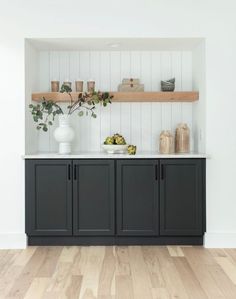 a kitchen with white walls and black cabinetry, wooden flooring and open shelving