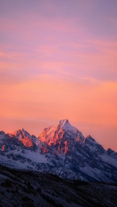 the mountains are covered in snow as the sun goes down on them and it is pink