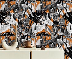 an orange and black floral wallpaper with white flowers on the sideboard next to a vase