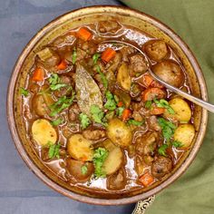 a bowl filled with meat and potatoes on top of a green cloth next to a spoon