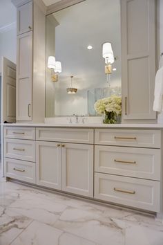 a bathroom with marble floors and white cabinetry, two lights on the wall and a large mirror over the sink