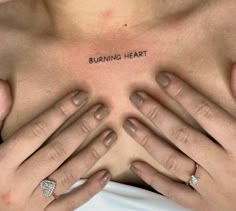 a woman's chest with the words burning heart tattooed on her left breast and two hands holding it