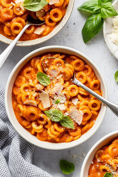 two bowls of pasta with basil and parmesan cheese on top, sitting next to each other