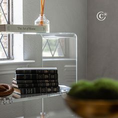 a stack of books sitting on top of a glass shelf next to a bowl of fruit