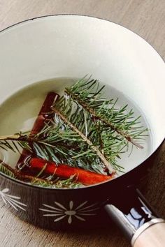 a pot filled with carrots and herbs on top of a wooden table next to a knife