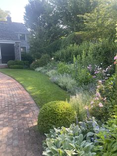 a brick path leading to a house surrounded by greenery and flowers in the foreground