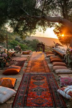 an outdoor seating area with lots of pillows and rugs on the ground at sunset