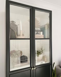 a black cabinet with glass doors and plants in the front, on a white wall