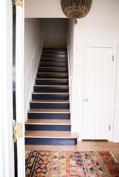 an open door leading to a set of stairs with rugs on the floor and a chandelier hanging from the ceiling