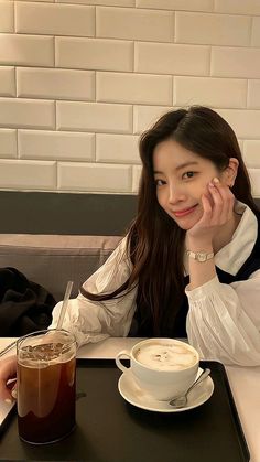 a woman sitting at a table with a cup of coffee in front of her and a drink on the side