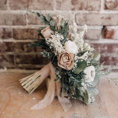 a bridal bouquet with flowers and greenery sits on a wooden table in front of a brick wall