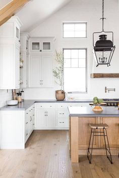 an open kitchen with white cabinets and wood flooring is seen in this image, the island has two stools on it