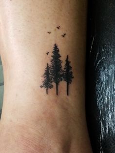 a small tattoo on the ankle of a woman's foot with trees and birds