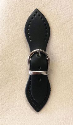 a black leather belt with metal buckles on the bottom and sides, sitting on a white surface