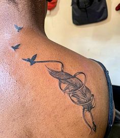 the back of a man's neck with birds flying around it and an arrow tattoo on his left shoulder