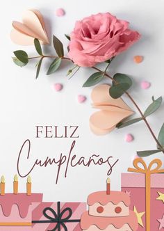 a pink rose sitting on top of a table next to cakes and gifts with the words feliz cumpleanos written in spanish