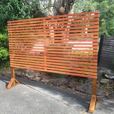 a wooden slatted screen sitting on the side of a road next to a tree