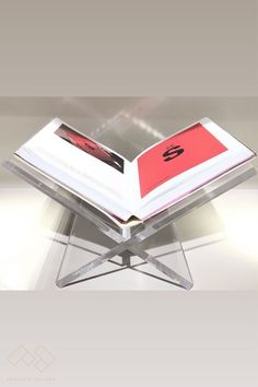 an open book sitting on top of a glass stand with a red cover and black logo