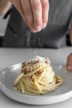 a person sprinkling parmesan cheese on top of pasta