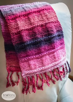 a pink and blue blanket sitting on top of a white couch next to a pillow