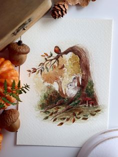 a card with an image of two cats in the woods on it, surrounded by autumn leaves and acorns