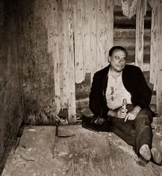 a man sitting on the floor in front of a wooden wall holding a beer bottle