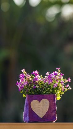 purple flowers in a heart - shaped vase with burlap and jute paper