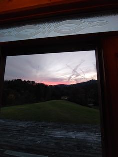 an open window looking out onto a field with mountains and trees in the background at sunset