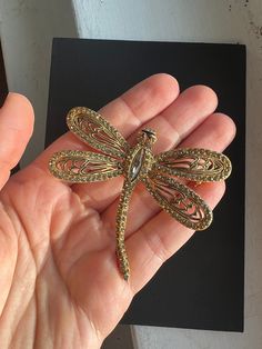 Vintage Vogue Jewelry Large Gold Tone RHINESTONE DRAGONFLY BROOCH. This dragonfly is outlined with small rhinestones with one large rhinestone as part of it's body. It's eyes are red rhinestones. The gold between it's wings are painted black. It is marked Vogue Jlry. Collectible Gold Brooches With Rhinestones, Ornate Jeweled Gold Brooches, Vintage Gold Brooch With Bling, Vogue Jewelry, Vintage Green Rhinestone Brooches, Gold Flower-shaped Rhinestone Brooches, Red Rhinestone, Vintage Vogue, Brooch Pin