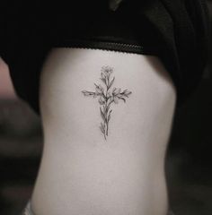 a cross tattoo on the back of a woman's lower body, with flowers growing out of it