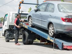 a man standing next to a car on the back of a flatbed tow truck